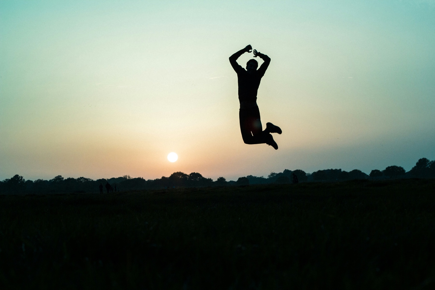 A person jumping high in a field at sunrise.