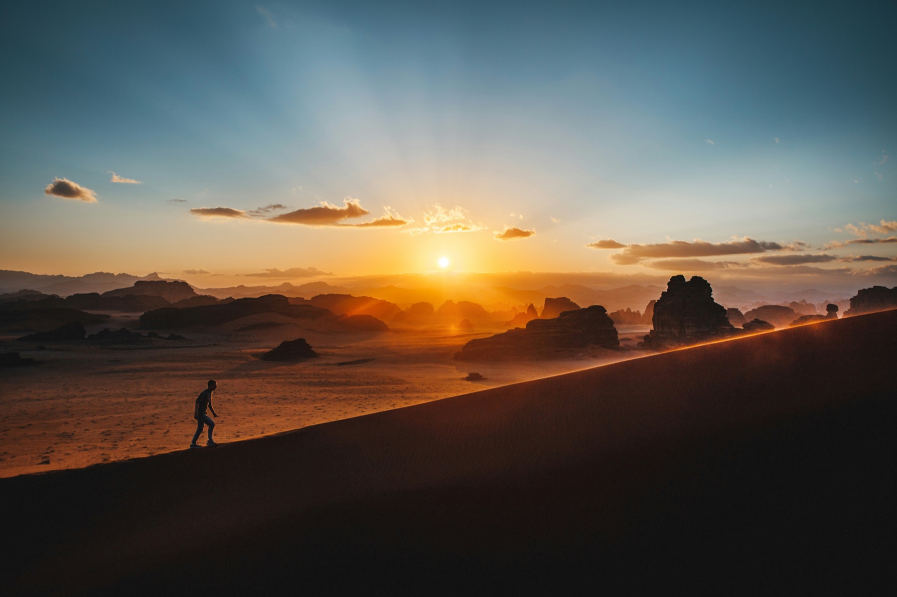 A person walking through a desert landscape at sunrise.