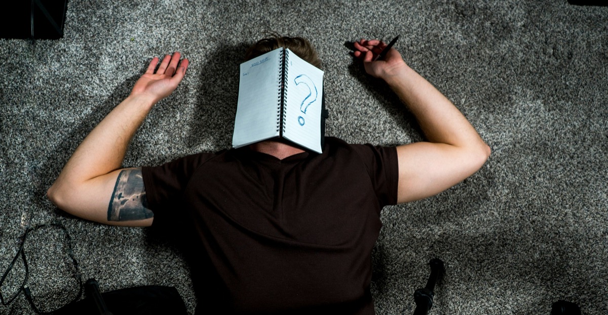 A person lying down with a notebook showing a question mark.